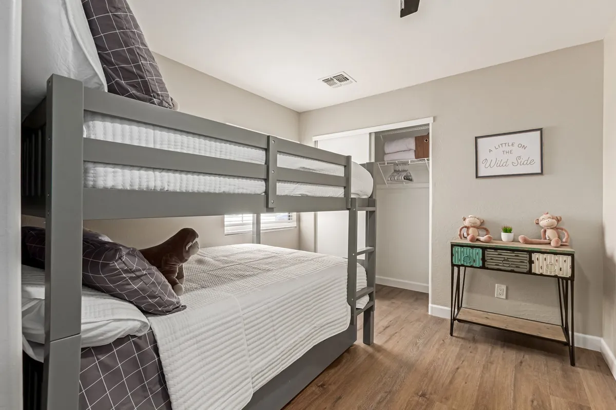 A cheerful bedroom designed for sharing, with a bunk bed, decorative wall art, and a nightstand topped with stuffed animals. The room exudes a playful mood, suggesting an inviting space for children or friends, while still feeling cozy and organized.