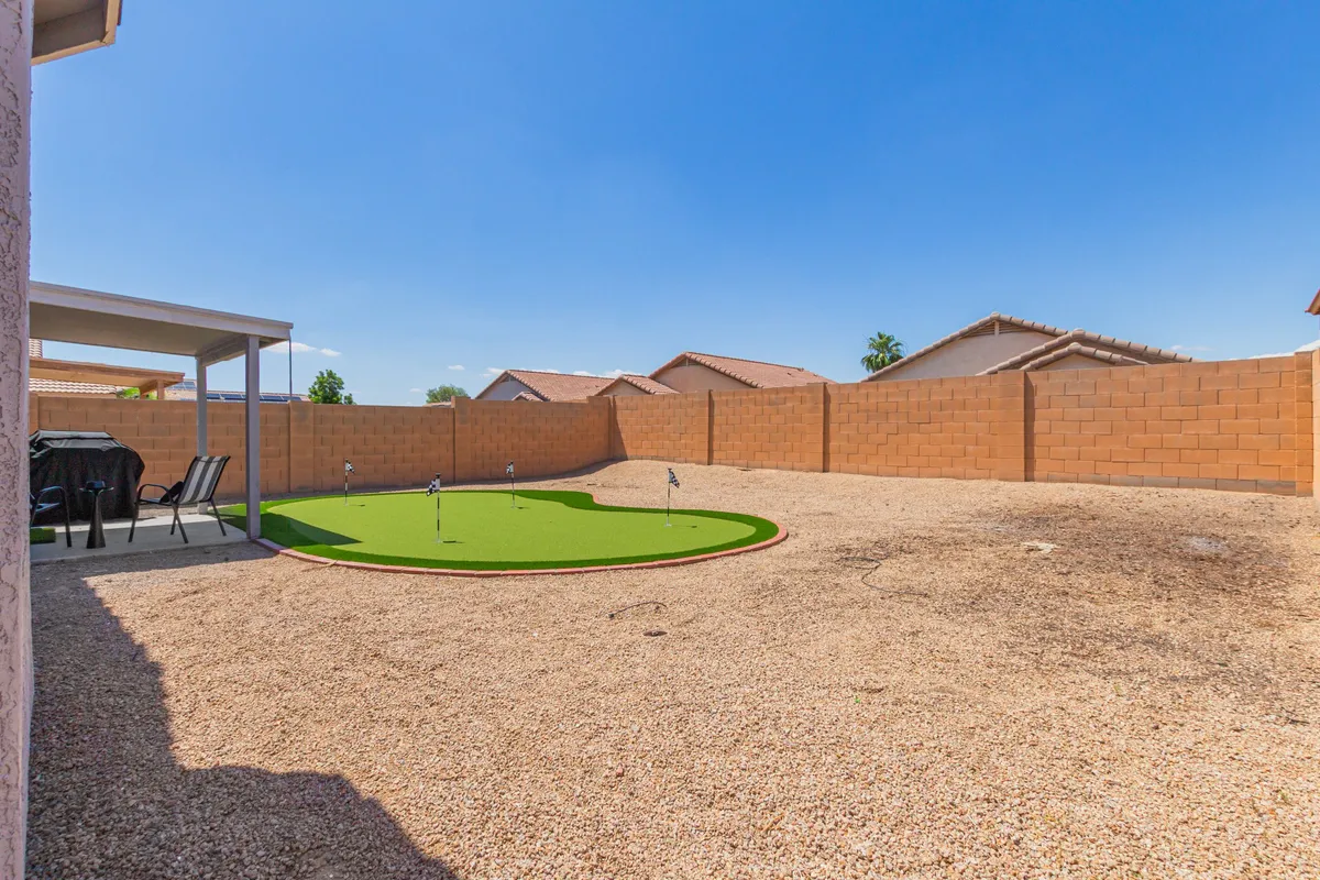 This exterior image features a neatly landscaped artificial putting green surrounded by a gravel surface and a comfortable patio area. Lounge chairs and outdoor seating suggest a space for gatherings and relaxation. The bright, open setting highlights opportunities for leisure and outdoor enjoyment right at home.