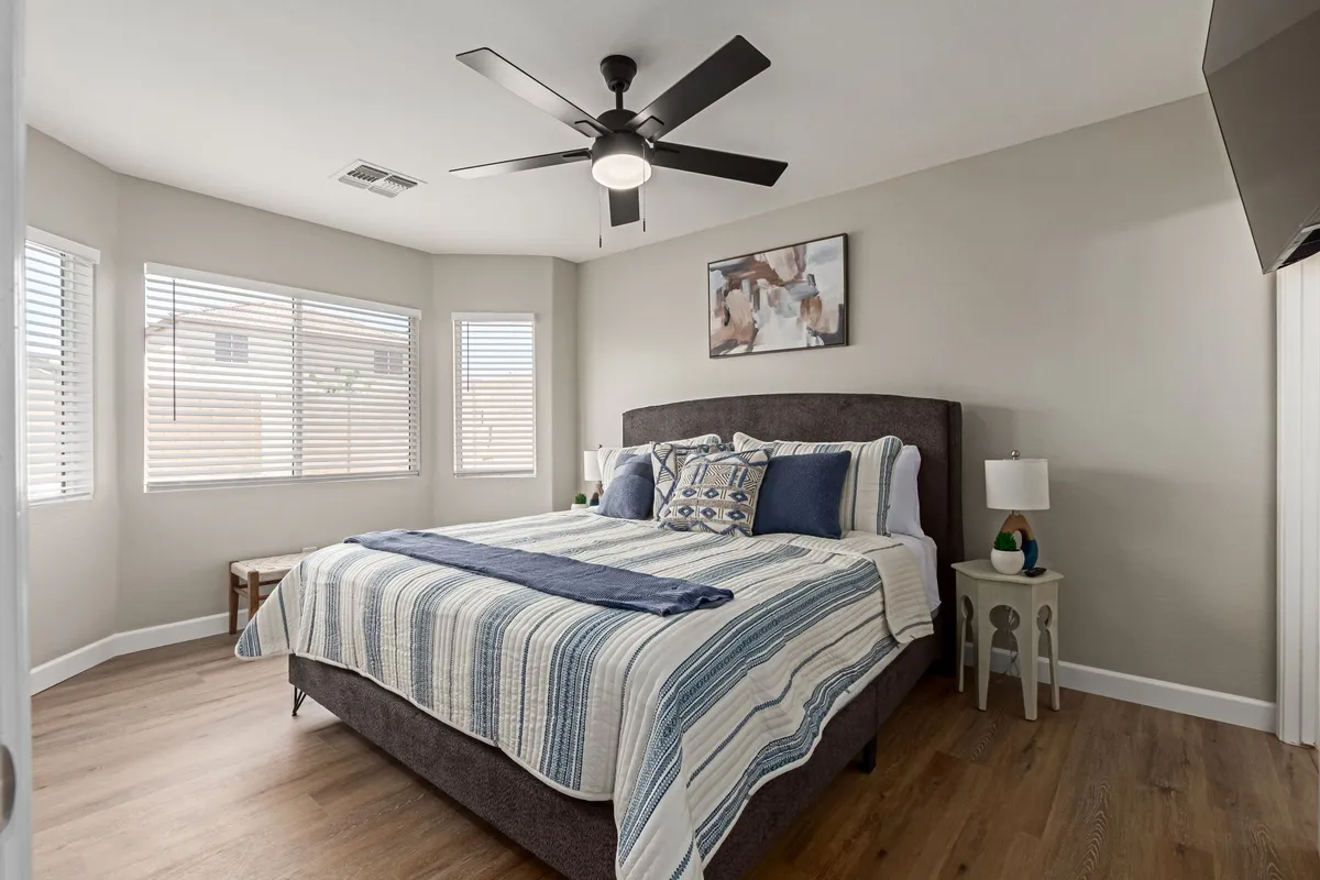 A serene secondary bedroom with a neatly made bed, cozy blankets, a nightstand with lighting, inspiring artwork, and large windows allowing natural light to stream in. The atmosphere is calm and restful, ideal for unwinding after a long day.