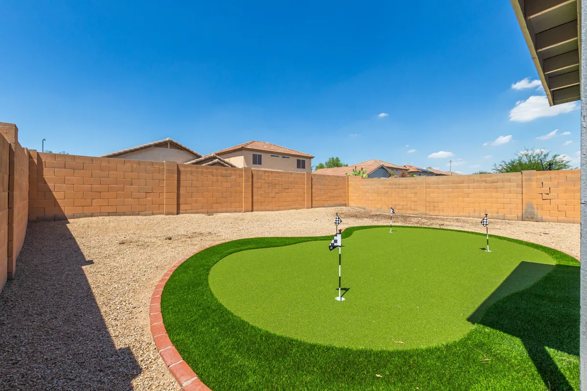 This exterior image features an artificial putting green bordered by low walls, under a bright blue sky. The scene is playful and inviting, suggesting opportunities for outdoor golf practice and gatherings.