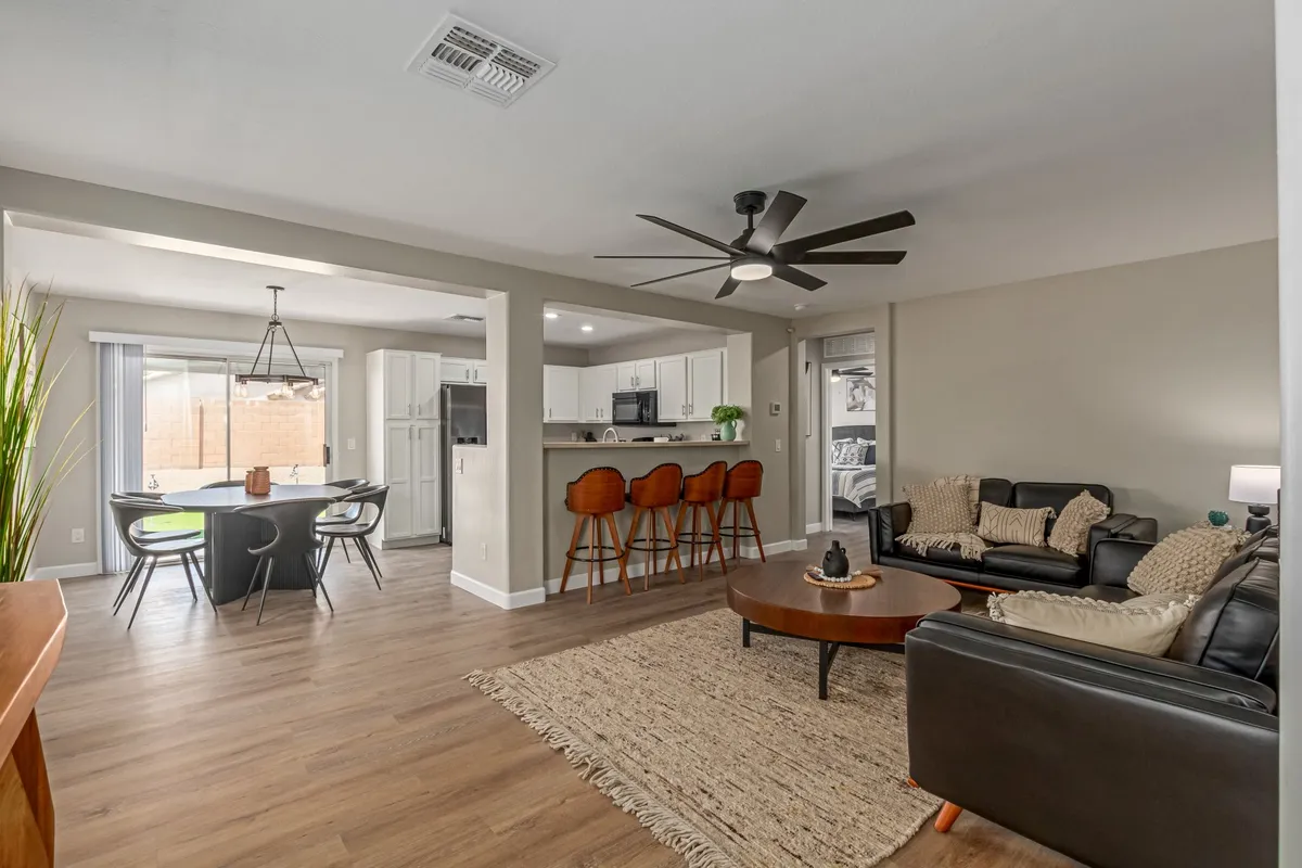 A bright, spacious living room seamlessly flows into a kitchen and dining area. The living room features comfortable seating, a cozy atmosphere, and a layout that encourages gathering and conversation. Sunlight pours through the windows, illuminating the entire open-concept space.