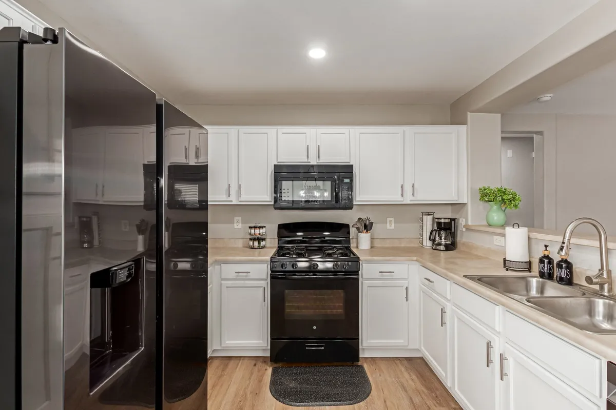 This image showcases a welcoming kitchen with a black refrigerator, white cabinetry, a stainless steel stove, and a kitchen sink. The layout is open and functional, perfect for cooking and gathering. The atmosphere is lively and inviting, capturing moments of meal preparation and social interaction.